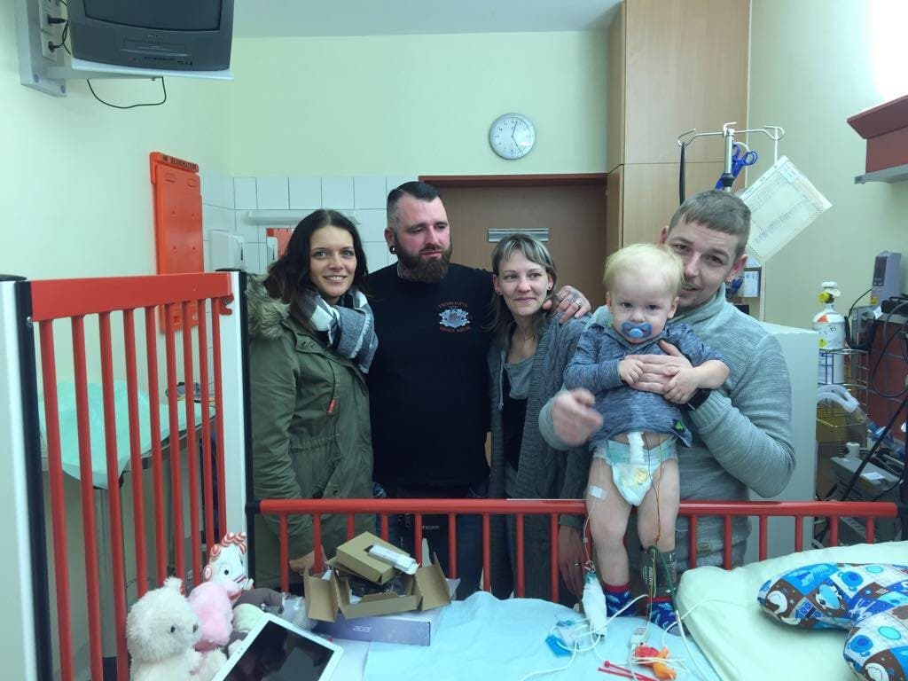 Vereinsmitglieder mit einer Familie am Kinderbett im Krankenhaus