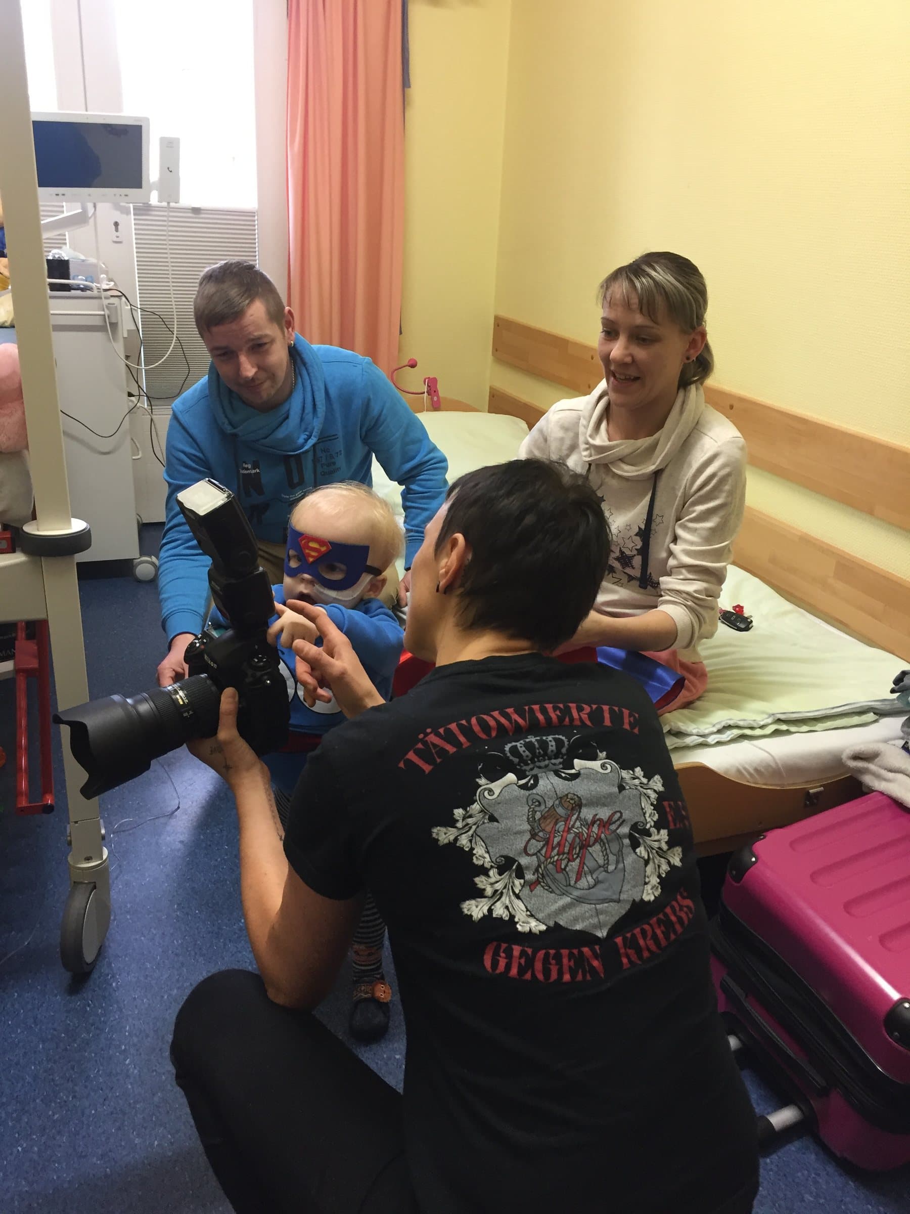 Ein Vereinsmitglied fotografiert ein Kind mit Superhelden-Maske im Krankenhaus, umgeben von der Familie